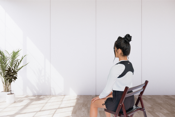 Woman sitting in a chair using a posture strap, how to improve posture 