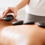 Masseuse doing hot stones massage to female client, placing stones on back, closeup