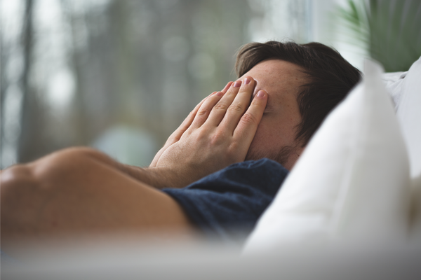 Young man with insomnia lying in bed and trying to sleep