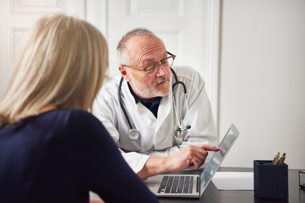 Senior medic in clinic explaining and consulting woman showing a laptop and sitting at the table.