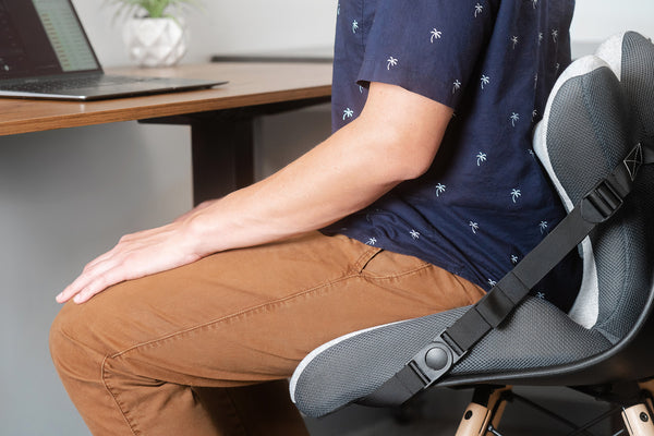 man sitting at a desk using a lumbar support cushion back pain office desk 