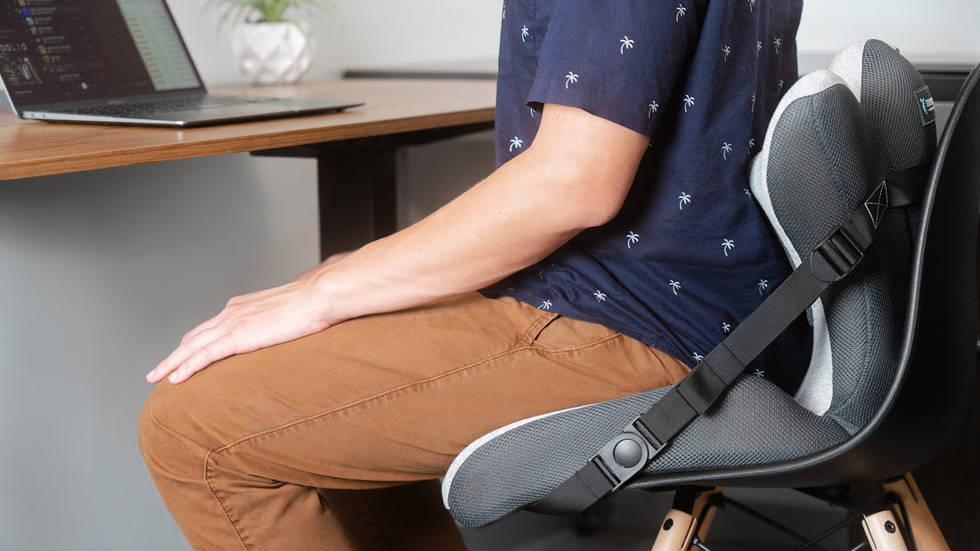 man sitting at a desk using a lumbar support cushion back pain office desk 