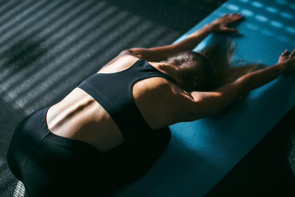 Beautiful young woman working out in gym, doing forward bend yoga exercise on blue mat, close-up