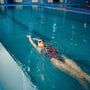 Female swimmer in swimsuit, cap and glasses swimming on her back in pool. The woman swims in the water, sport training, motion view