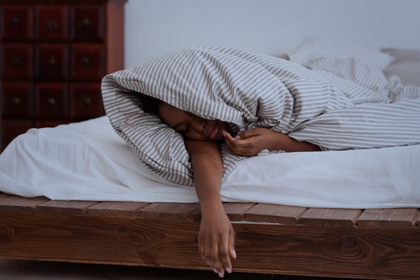 Getting enough sleep, deep sleep, trouble sleeping, problems and insomnia in night. Sad tired african american female in blanket sleeps on bed in interior of bedroom, dark, panorama, empty space