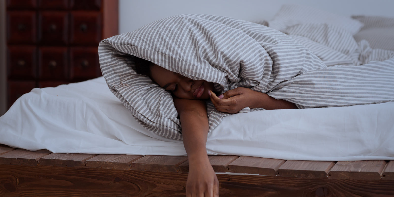 Getting enough sleep, deep sleep, trouble sleeping, problems and insomnia in night. Sad tired african american female in blanket sleeps on bed in interior of bedroom, dark, panorama, empty space