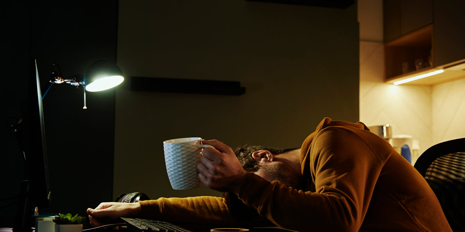 Man sleeping at home office workplace with cup of coffeee in his hand. Freelancer remotely working late. Emotional stress and burnout